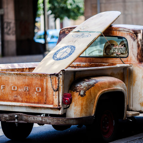 A surfboard in the back of an old Ford truck.