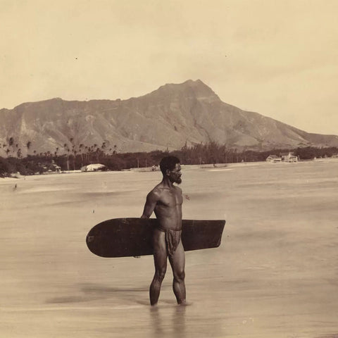A Native Hawaiian holding an alaia surfboard with Diamond Head in the background.