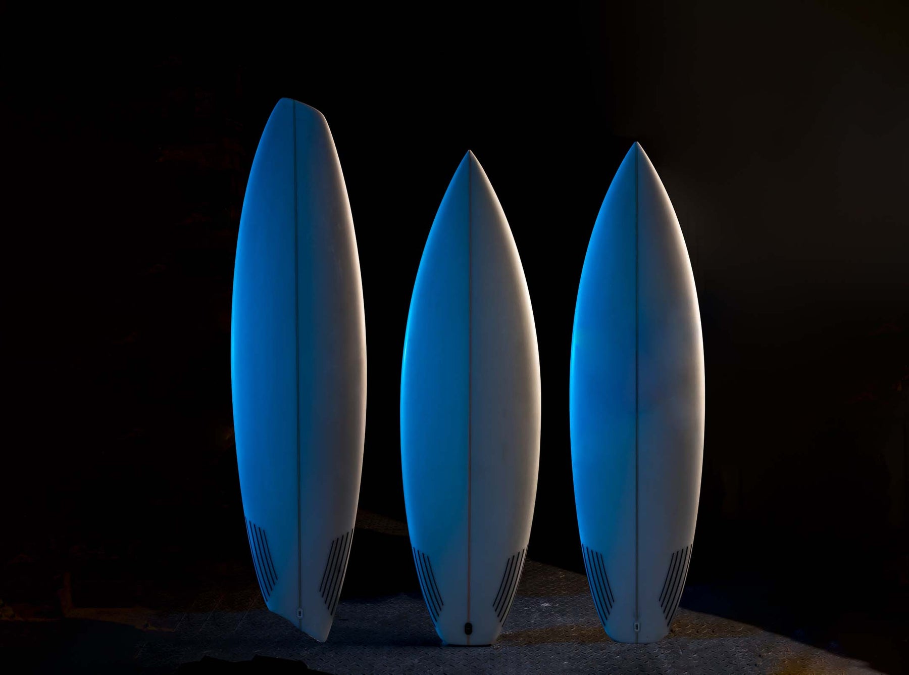 Three logo-less surfboards in blue light. 
