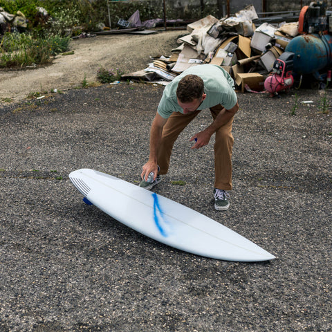 A man spray paints a surfboard. 