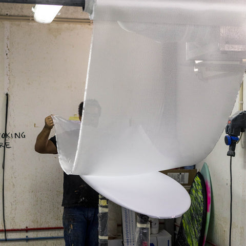 A man applying fiberglass cloth to a shaped surfboard blank. 