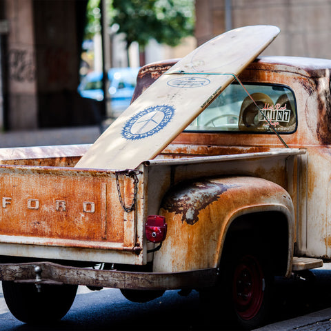 A surfboard in the back of an old Ford truck. 