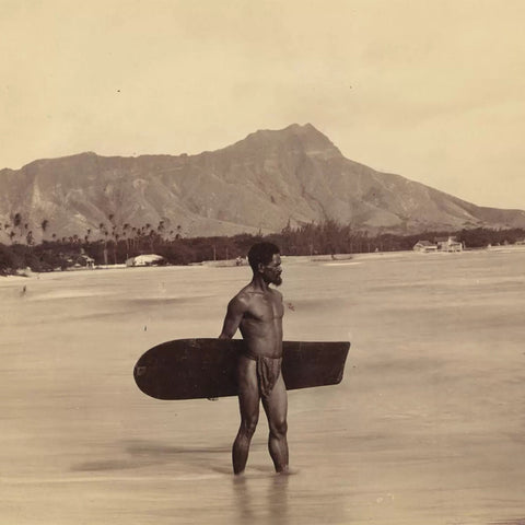 A Native Hawaiian holding an alaia surfboard with Diamond Head in the background. 